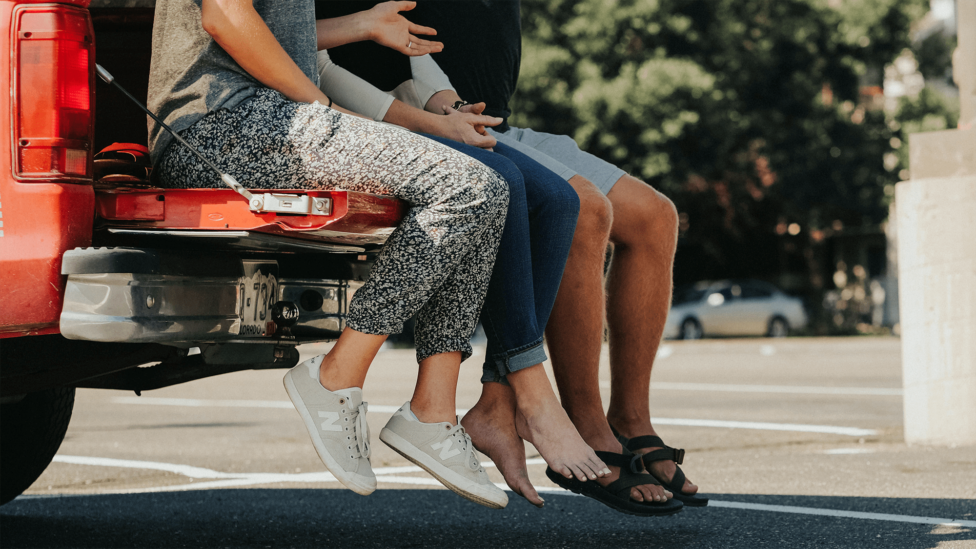 three people legs and shoes visible sitting on edge of car trunk