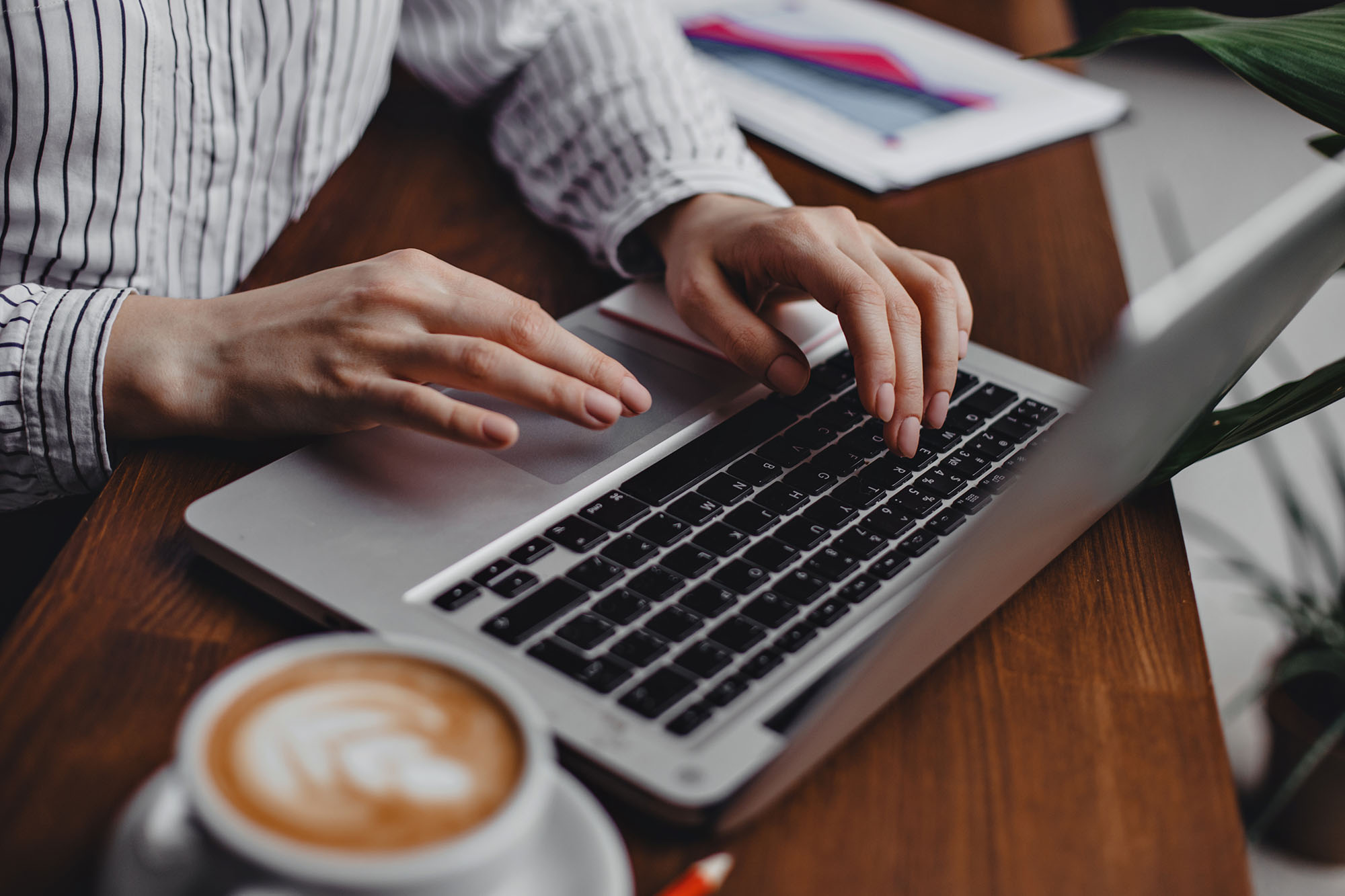 image of desk with laptop coffee cup and female hands typing