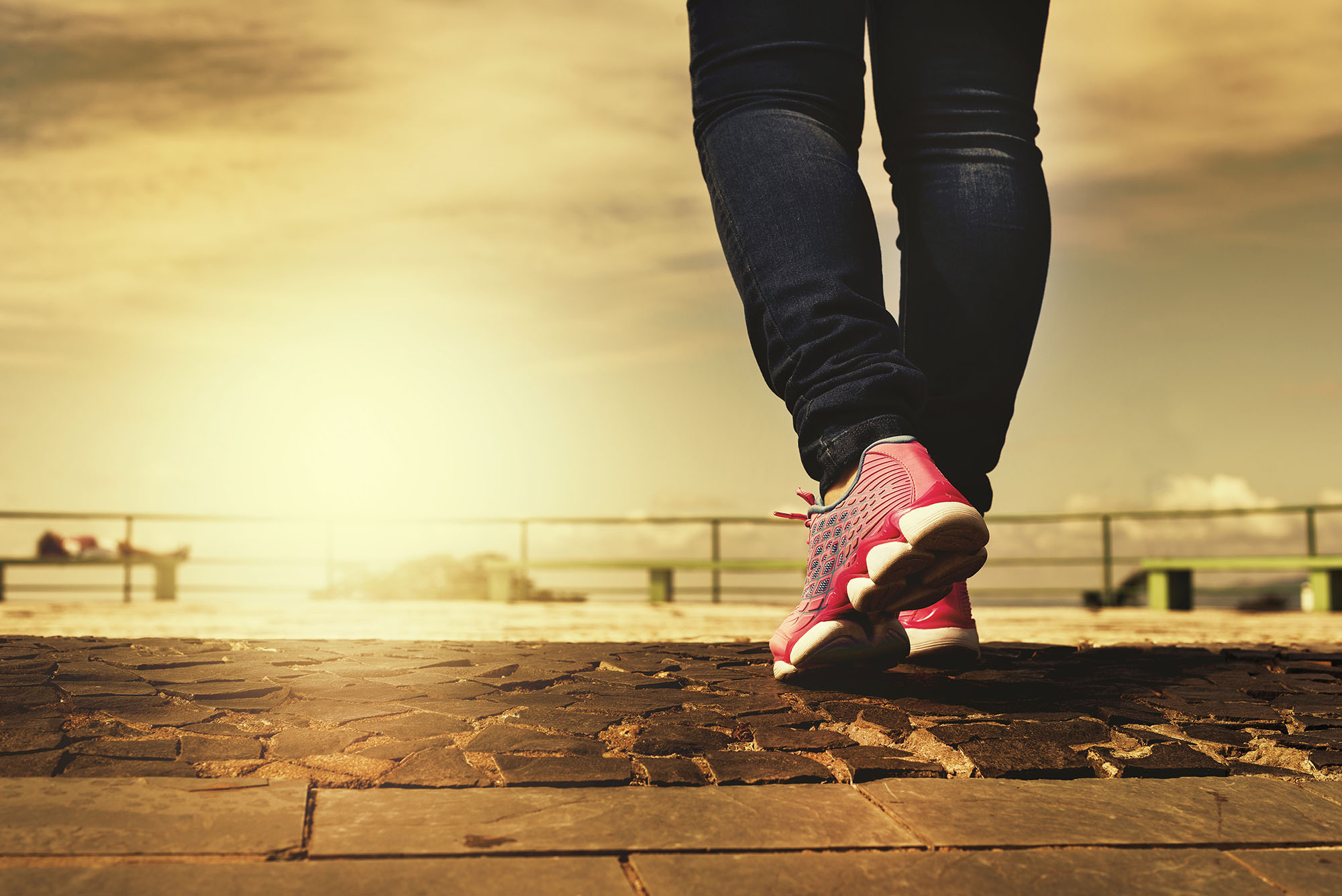 image of sunset and a pair of human legs in sports shoes walking