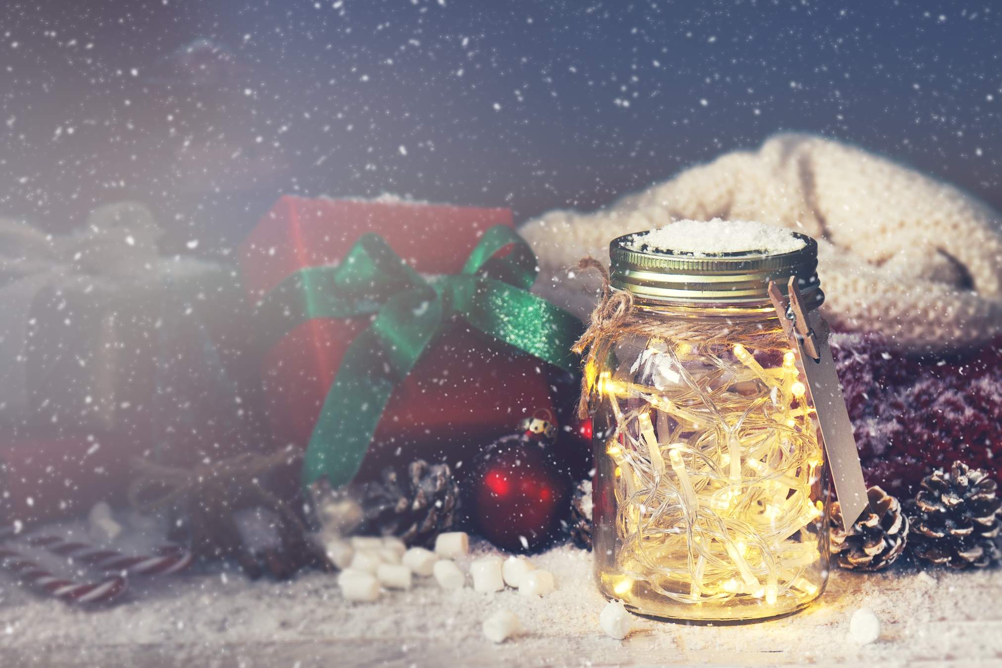 Fairy christmas holiday lights in a jar with christmas decoration and snow in half darkness