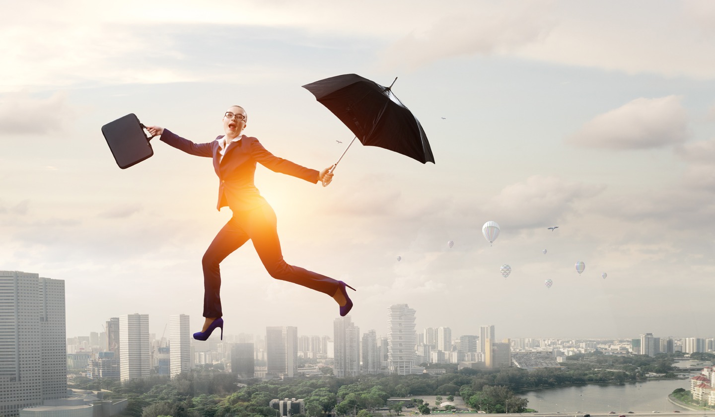 Young businesswoman walking with umbrella with skyline behind her to make her appear flying