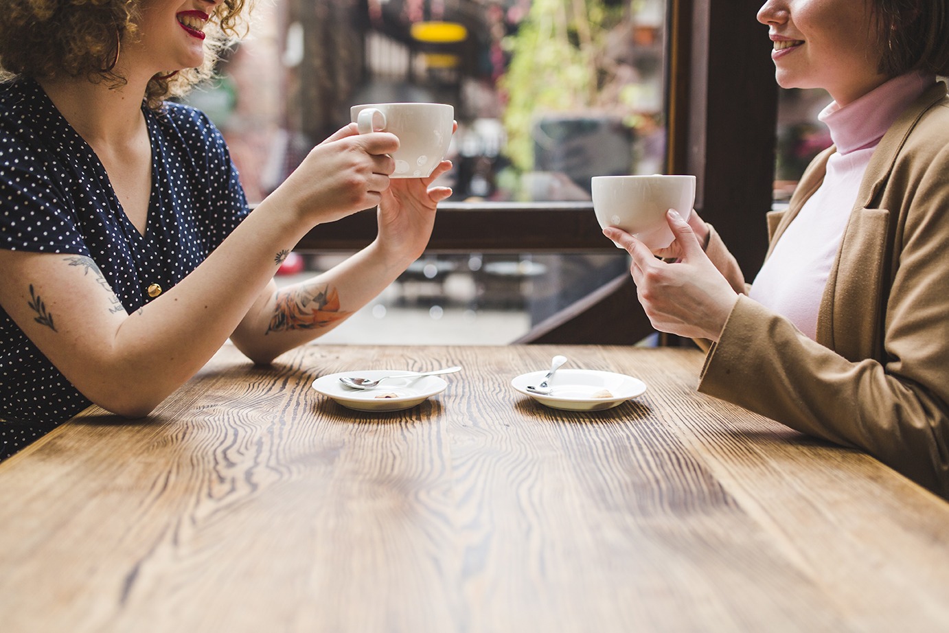 image of two women at cafe table drinking coffee smiling