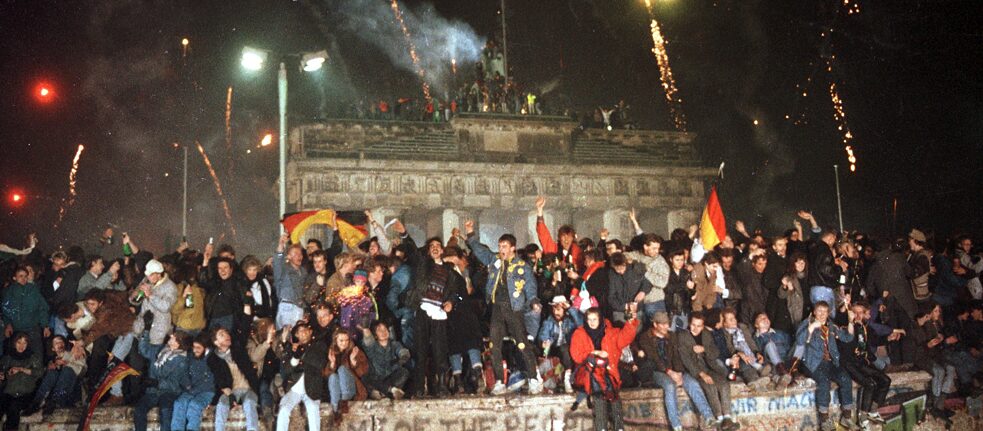 Photo von auf der Berliner Mauer feiernden Menschen, das Brandenburger Tor im Hintergrund.