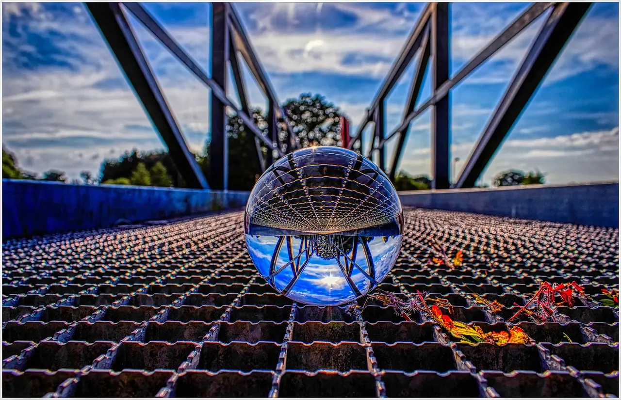 Image of a bridge and some weeds growing through the iron grill parapet, with a glass sphere reflecting the image upside down.