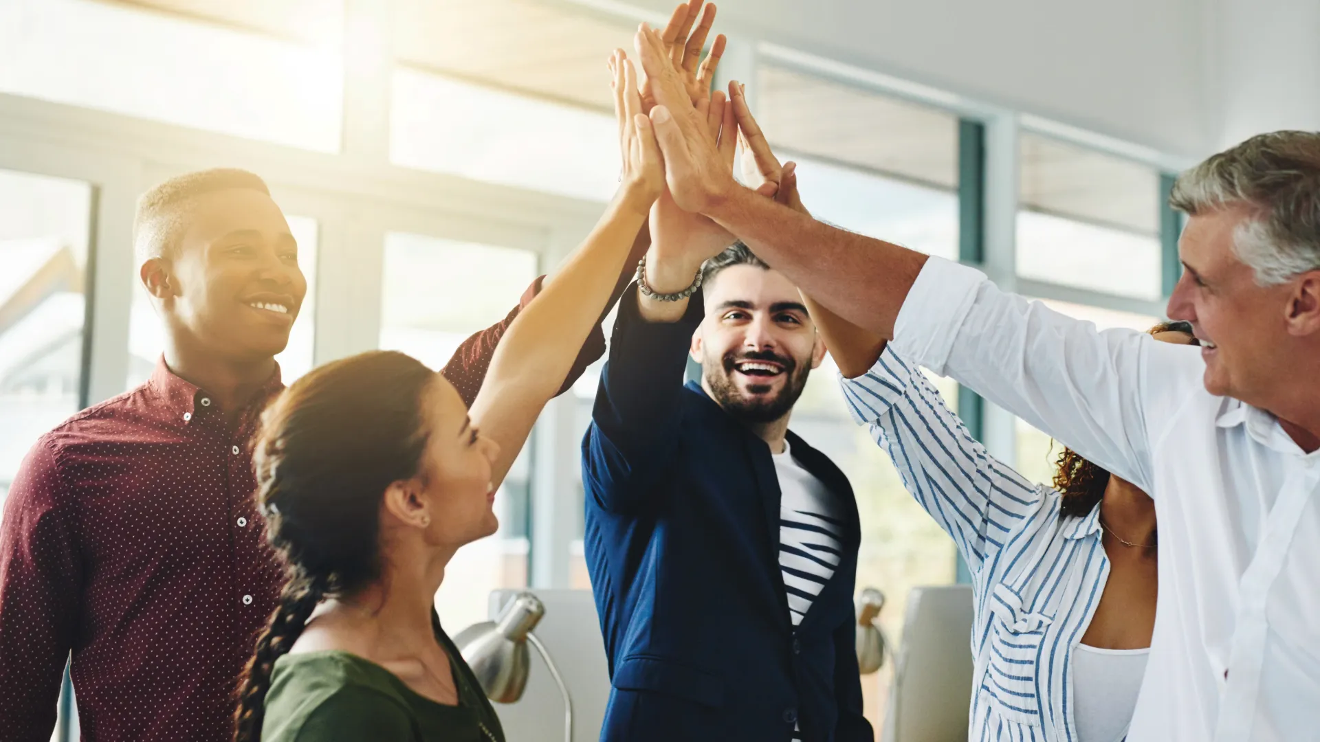 A group of people smiling and joining hands standing in a circle, all colours, ages and gender.