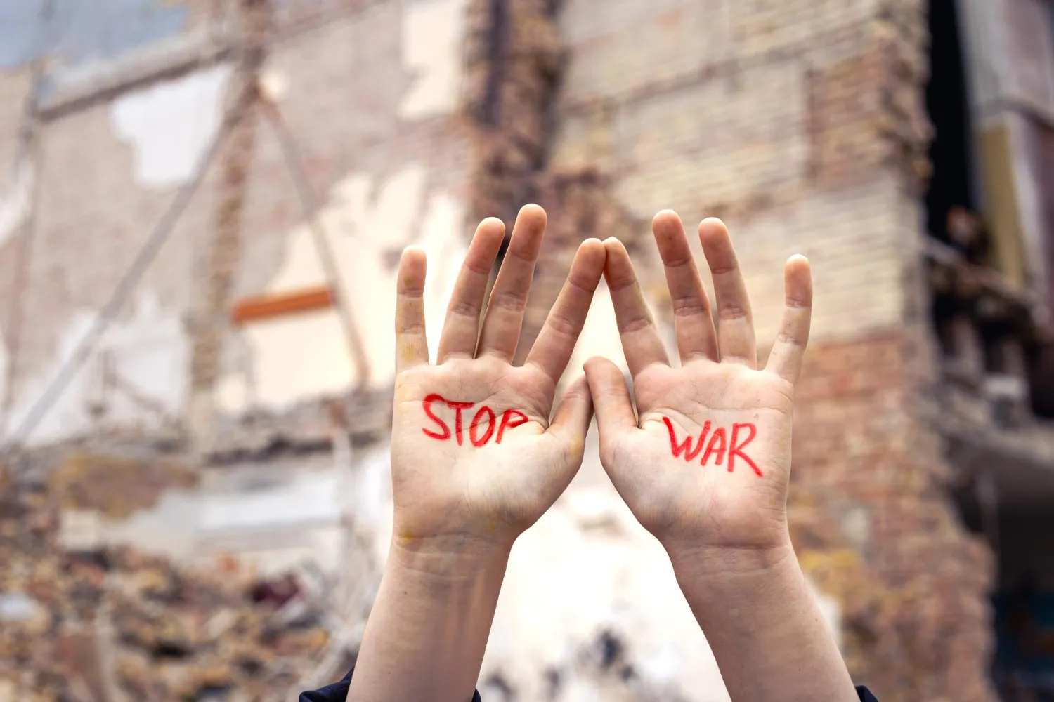 A house in ruins and befor it the two hands of a person held up, showing the words stop war written in red coloour on them.