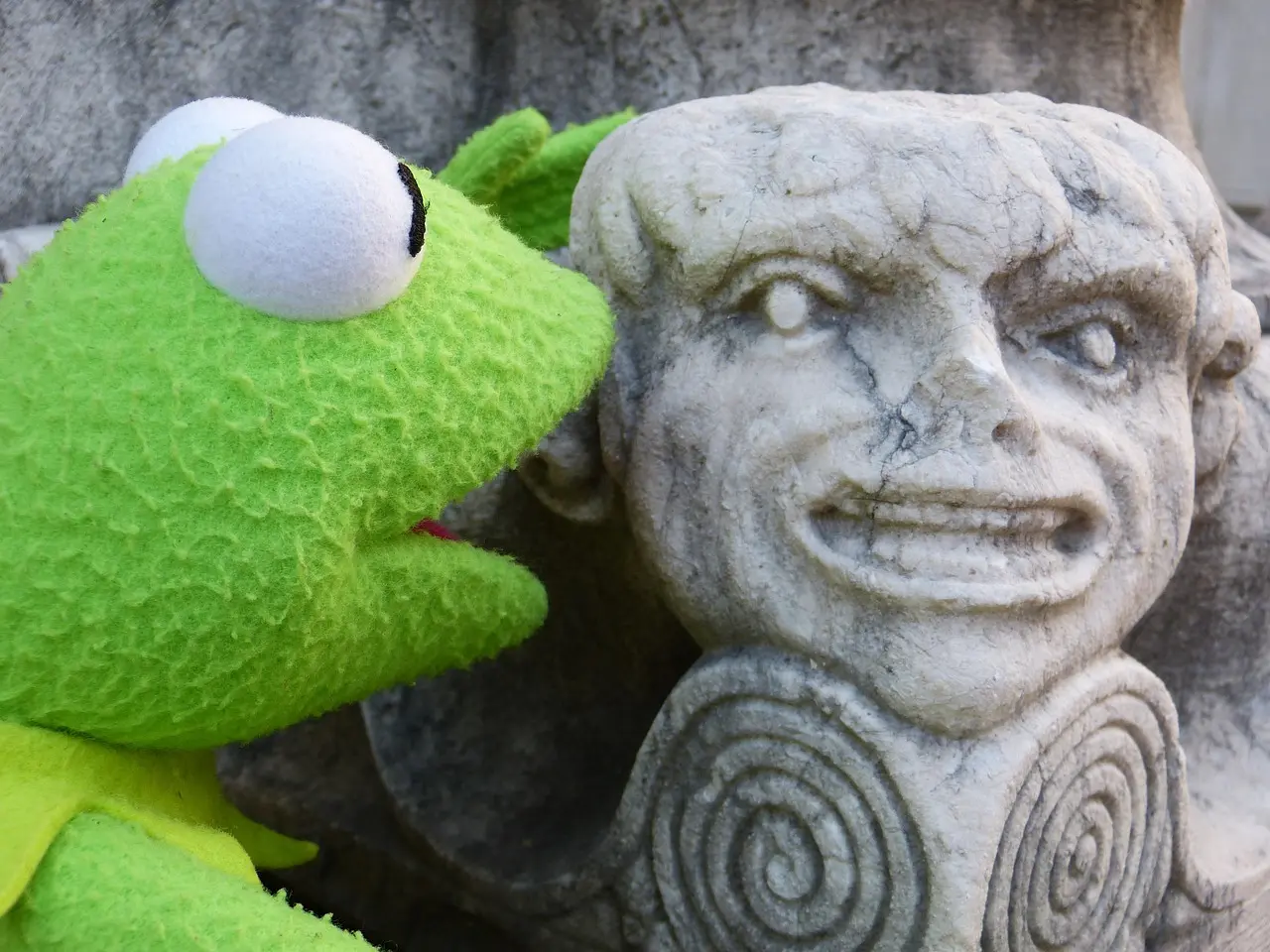 Puppet character Kermit the frog talking to a stone figure looking like a smiling woman.
