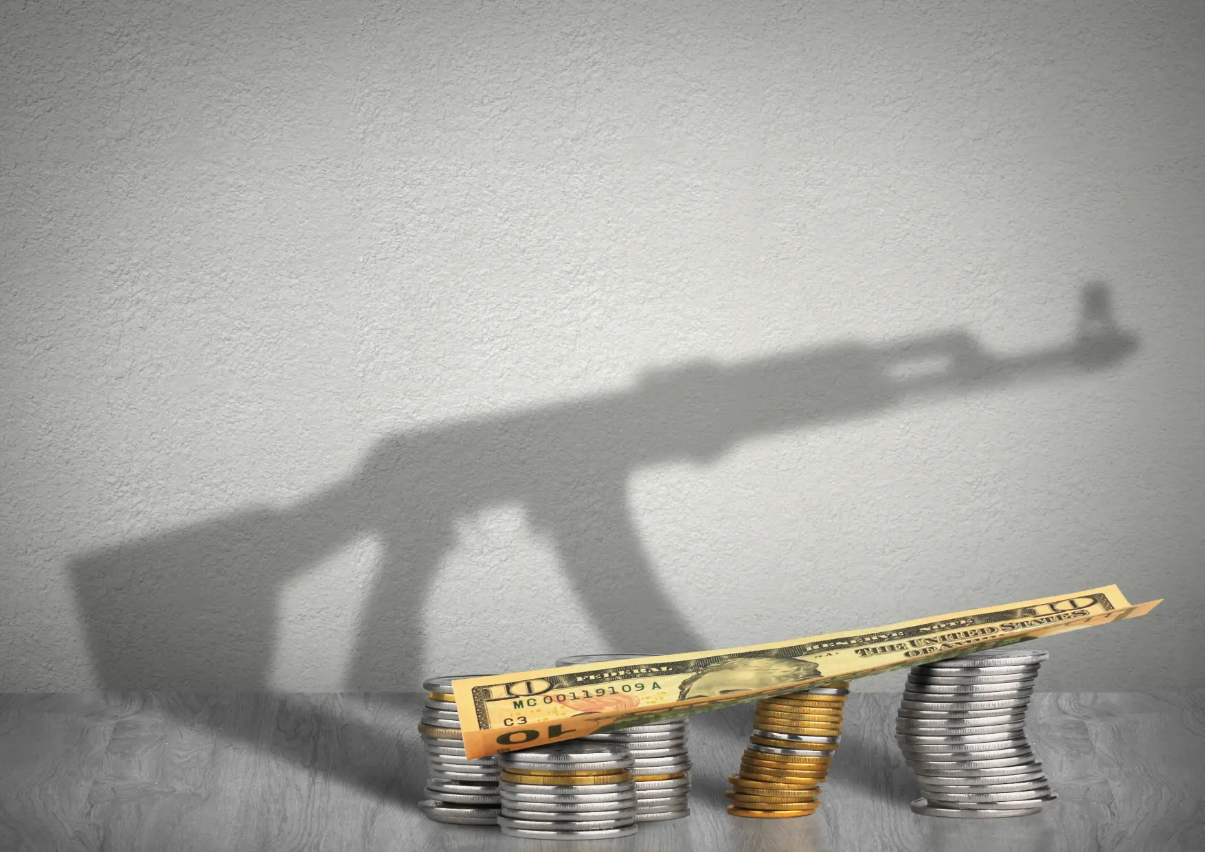 Coins and a money bill in front with a shadow behind them that is the shape of a gun.