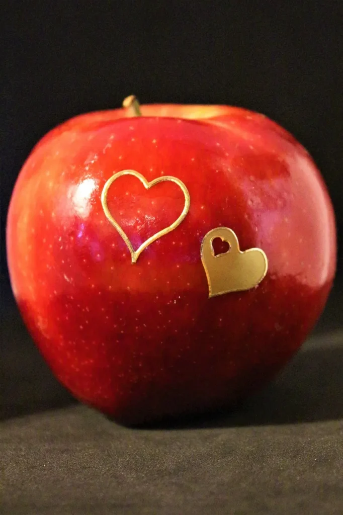 red shiny apple with two golden heart shapes printed on it.